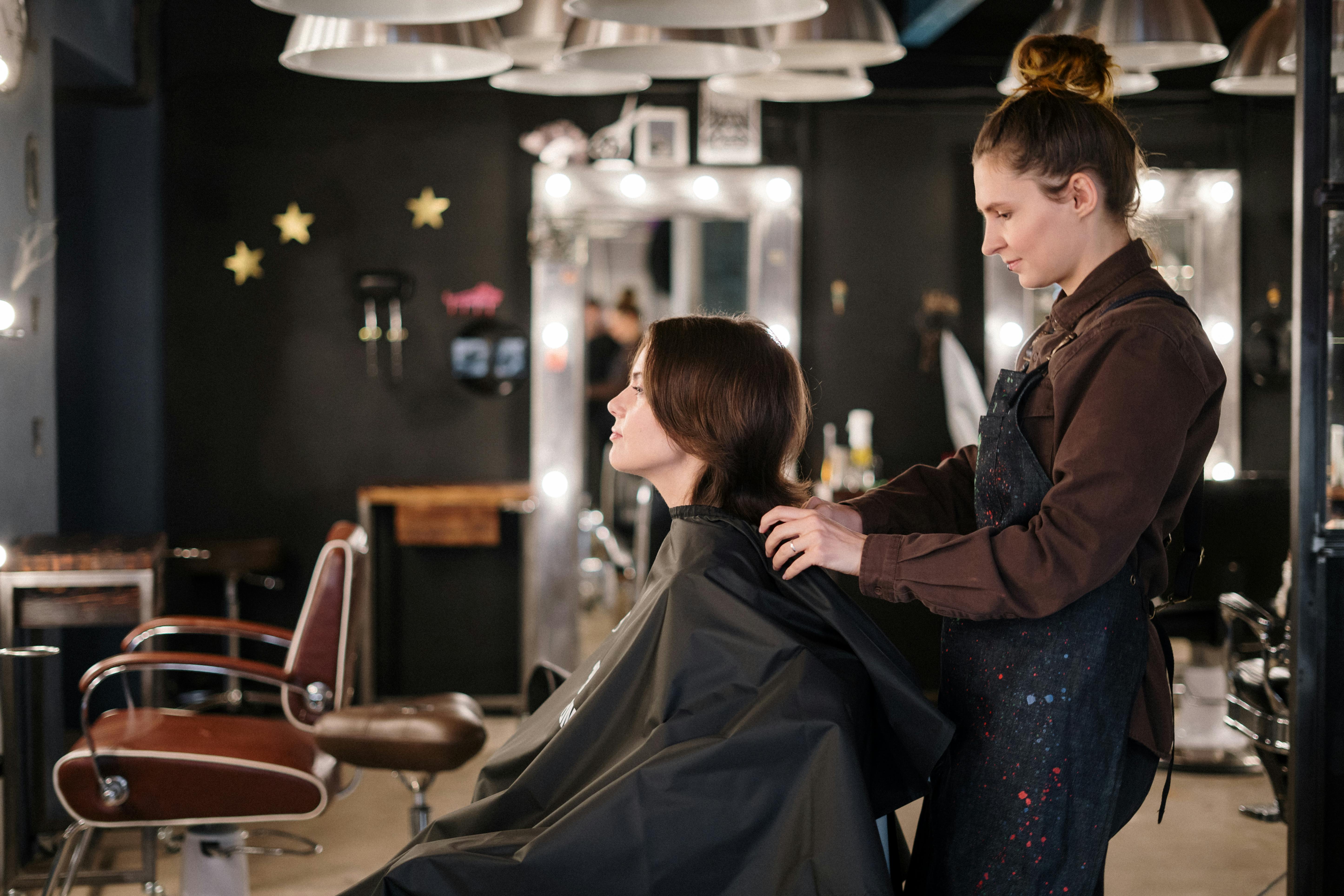 Stylist working on client's hair in a moody salon with warm pendant lighting